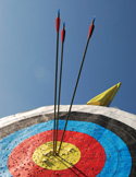 Low-angle view of three arrows clustered in the yellow bullseye of a colorful archery target.