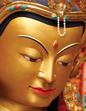 Close-up of a golden Buddha statue face with colorful jewels and serene expression.