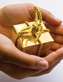 Two hands gently holding a small, decorative gold gift box tied with a gold cord.