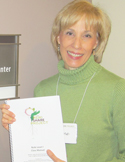 A smiling woman in a green sweater holding a "Reiki Share Project" manual.