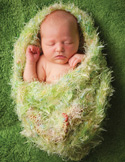 A sleeping newborn baby snugly swaddled in a soft, textured light green blanket on a green surface.