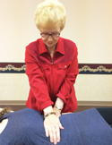 A woman in a red jacket performs a Reiki hand healing session on a person lying face down.