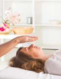 Close-up of a person receiving a Reiki treatment with hands hovering over their forehead in a bright room.