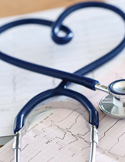 A blue stethoscope curled into a heart shape resting on top of medical EKG charts.