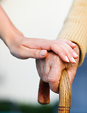 Close-up of a young hand gently resting on an elderly hand that is holding a wooden walking cane.