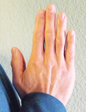 Close-up of a person's hands pressed together in a prayer or Gassho position against a textured wall.