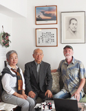 Three people sitting on a couch for an interview in a room with framed calligraphy and a portrait on the wall.