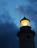Low-angle view of a lighthouse lantern room glowing bright yellow against a dark, cloudy twilight sky.