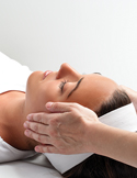 Close-up of a person lying down receiving a Reiki healing session with hands placed gently on their temples.