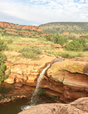 A narrow waterfall flows over red rock cliffs into a pool in the desert landscape of Sedona, Arizona.