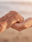 A close-up of a younger hand gently holding the weathered, wrinkled hand of an elderly person in a supportive gesture.