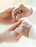 A close-up of a younger person's hands gently holding the weathered hands of an elderly person.