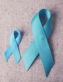 Two light blue awareness ribbons of different sizes resting on a textured, neutral-colored fabric surface.