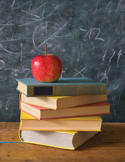 A red apple resting on a stack of colorful hardcover books in front of a chalkboard.