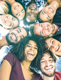 A diverse group of smiling young adults looking down into the camera lens in a tight circle.