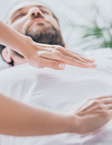 A close-up of a practitioner's hands hovering over a man's chest during a Reiki healing session.