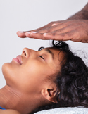 A practitioner’s hands hover over a woman's forehead during a calming Reiki energy session.