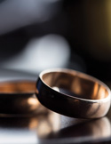 Close-up, shallow-focus shot of two gold wedding bands resting on a dark, reflective surface.