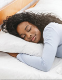 A woman with long curly hair sleeping peacefully on a white pillow and bedsheets.