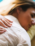 Close-up of a person’s hands resting gently on the back of a woman lying down during a healing session.