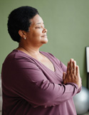 A woman with eyes closed and a peaceful expression, holding her hands together in a prayer or gassho position.