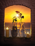 Two roses in glass vases on a stone ledge framed by a brick archway, with a sunset over the ocean behind them.