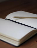 A close-up of a blank open notebook with a wooden pencil resting on the page.