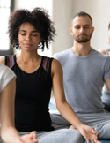 A group of people sitting with eyes closed in a peaceful meditation pose during a wellness class.