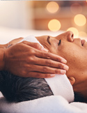 Close-up of hands gently resting on a person’s face during a relaxing Reiki or massage session.