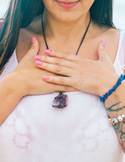A woman holds her hands over her heart center while wearing a large raw amethyst crystal necklace.