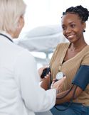 A doctor takes the blood pressure of a smiling woman during a medical checkup.