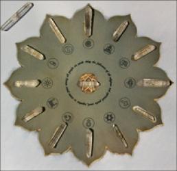 Circular, flower-shaped metallic display with embedded crystal-like pieces and various spiritual or symbolic icons arranged around the center.